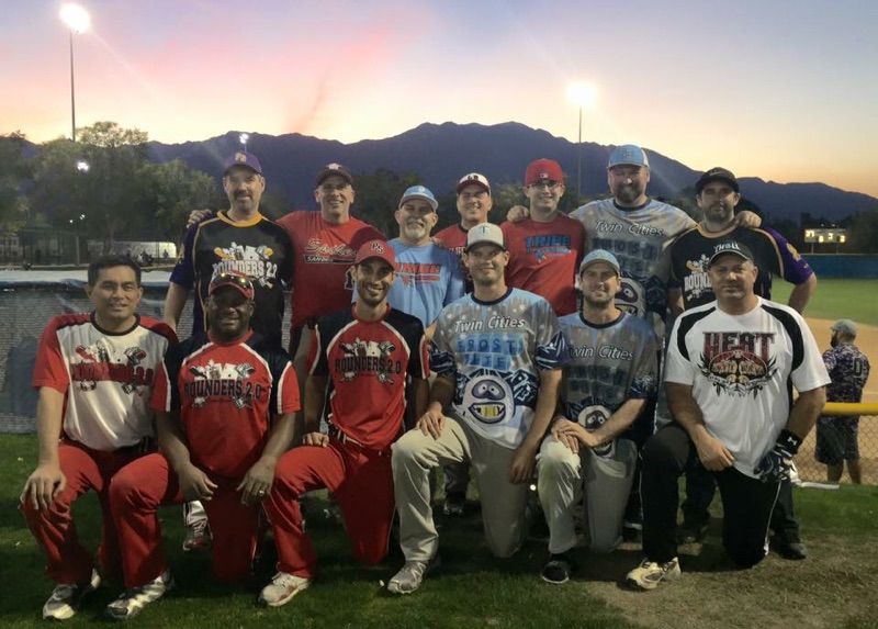 Group of baseball players posing on a field at sunset with mountains in the background.