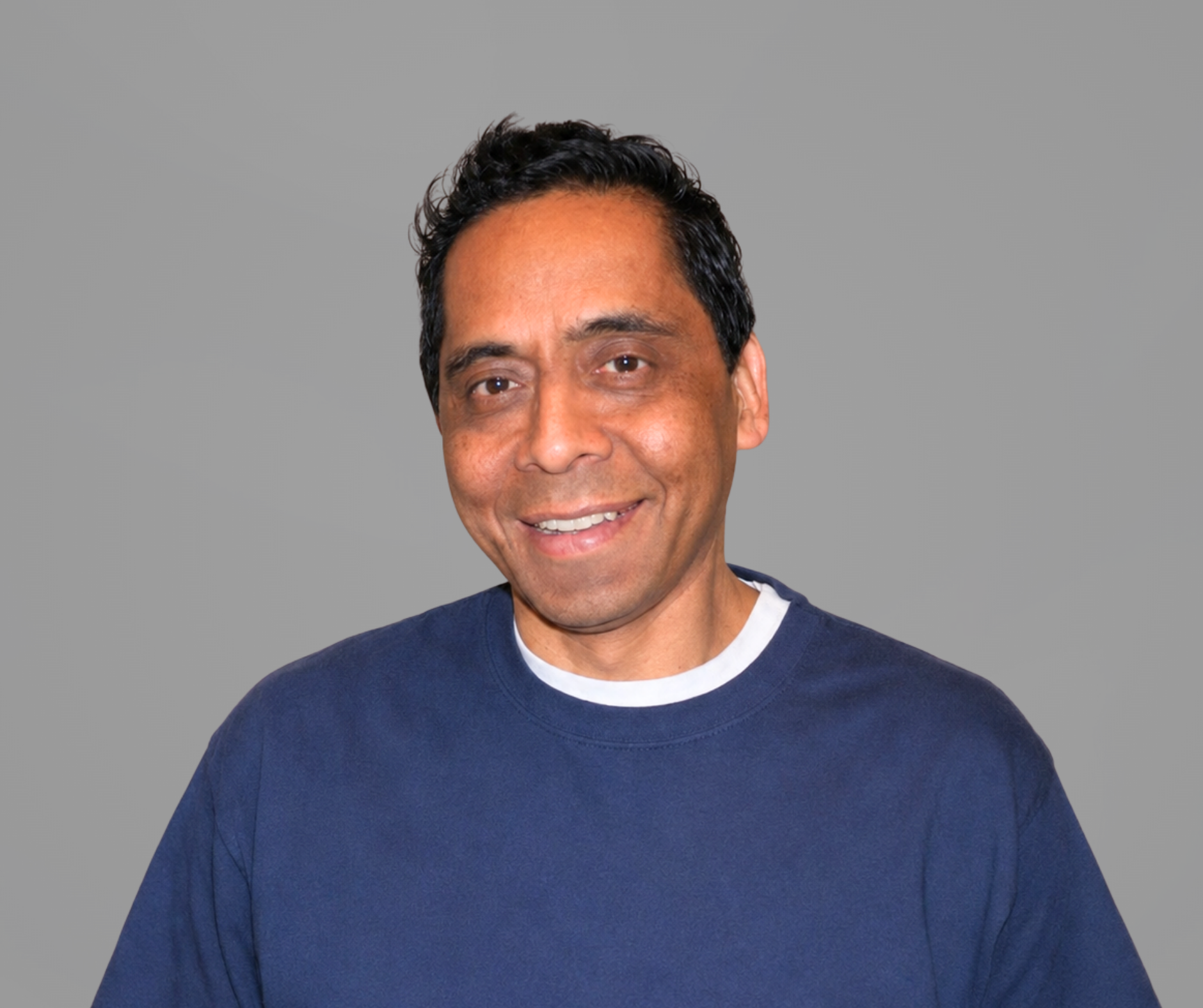 Headshot of Ross Benson, a man smiling, wearing a gray collared shirt, set upon a gray background.