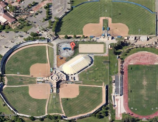 Aerial view of a baseball complex with three fields, a building, parking lot, and a red map pin.
