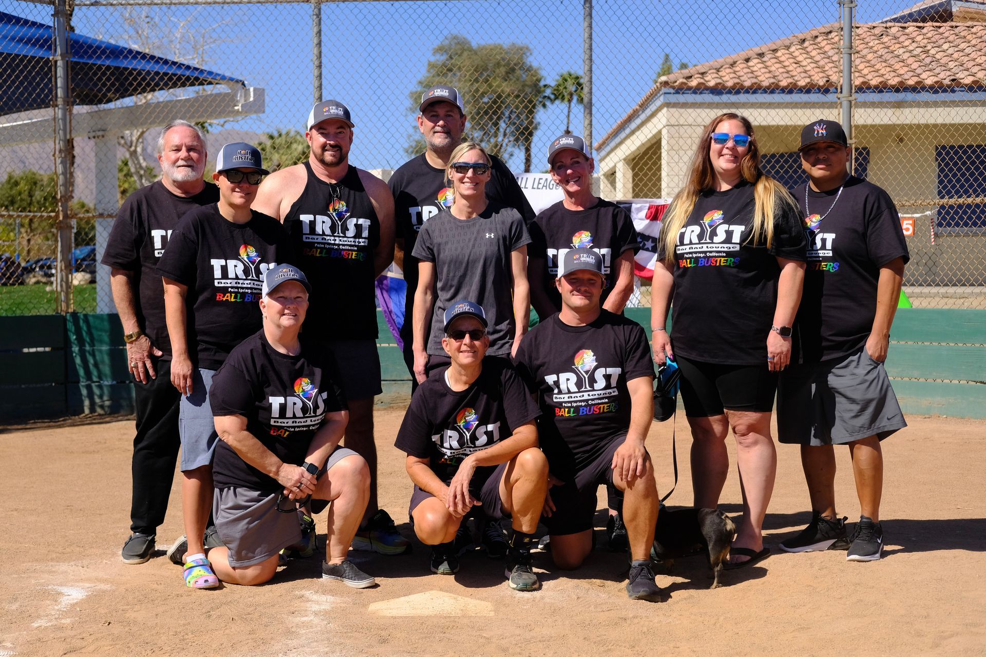 Group of softball players in black uniforms posing together on a dirt field