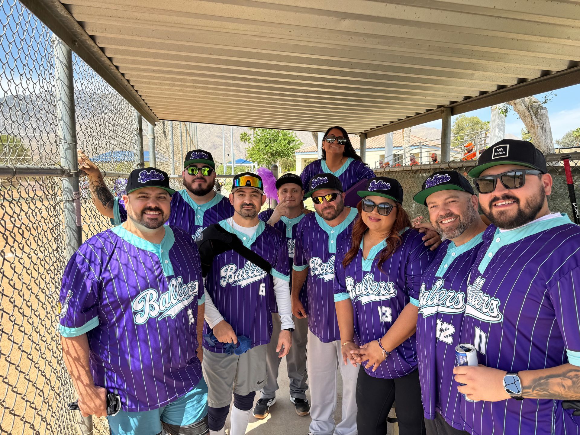 Group in purple jerseys posing under a shaded pavilion, smiling at the camera.