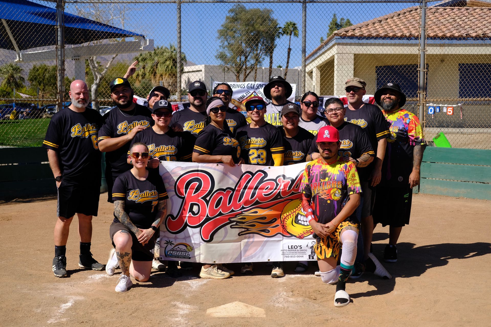 Youth softball team posing with a colorful championship banner on a sunny field.