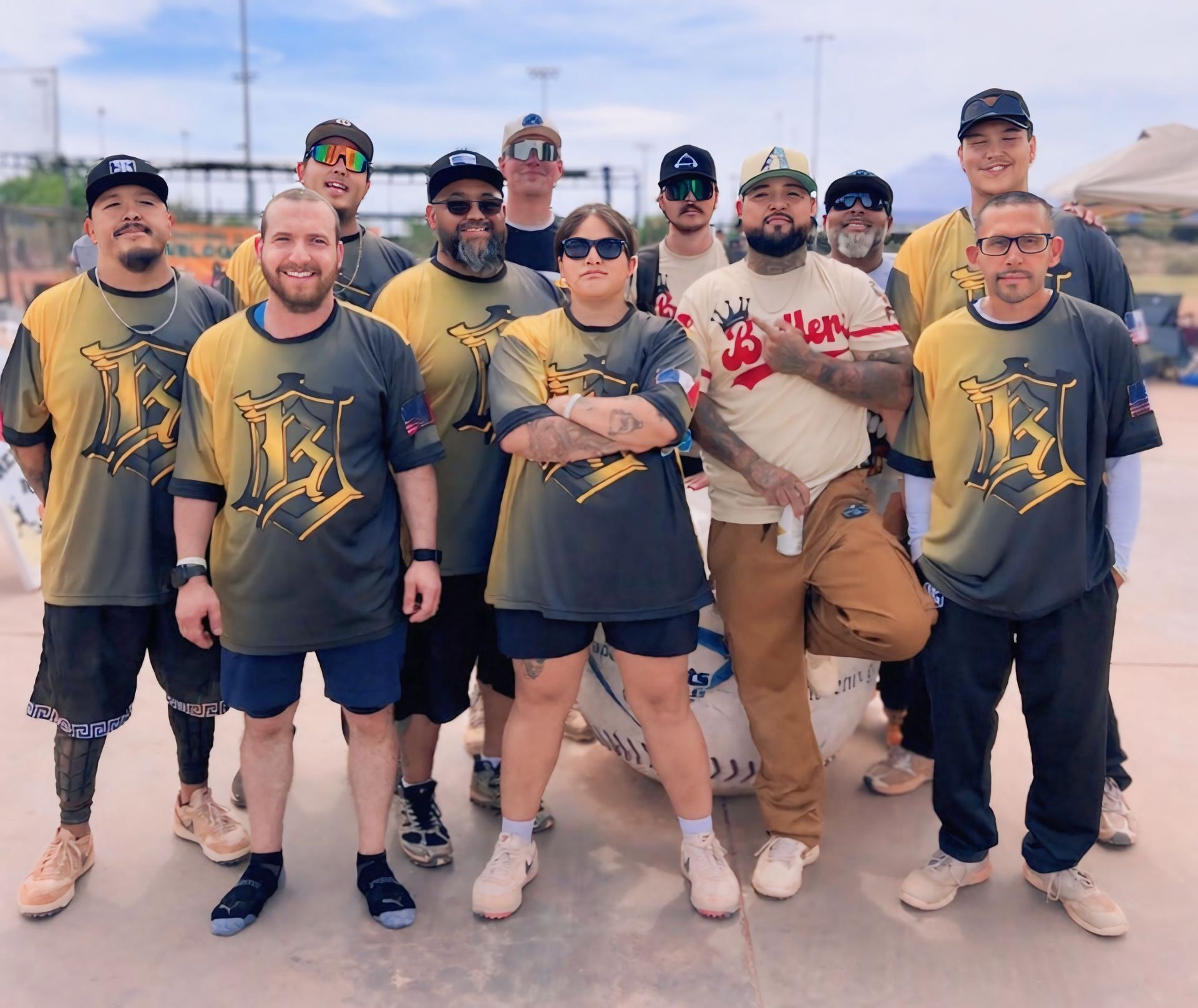 Group of people posing outdoors in matching baseball shirts and caps, smiling at the camera.