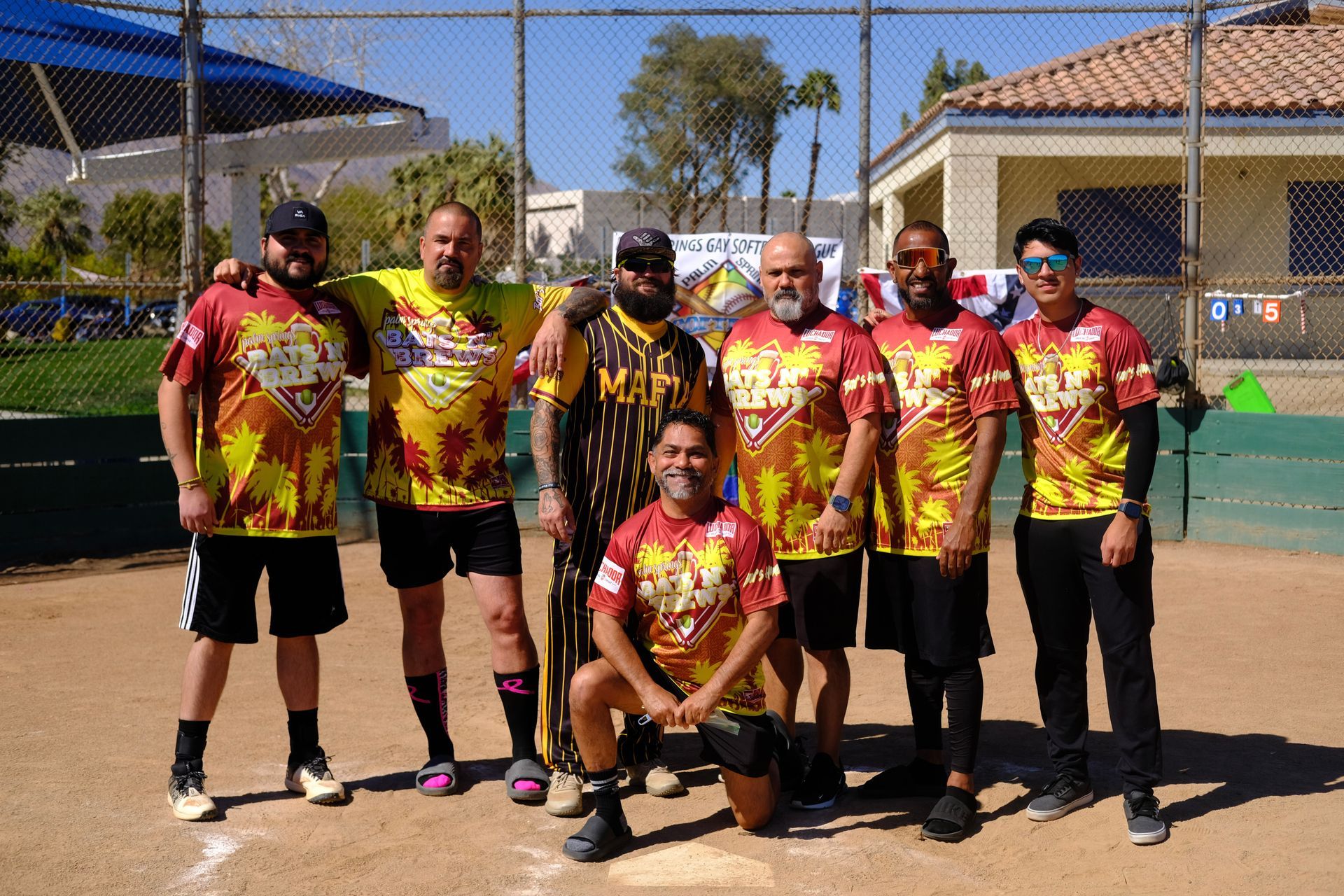 Softball team posing on a sunny field, wearing matching red-yellow jerseys and black pants