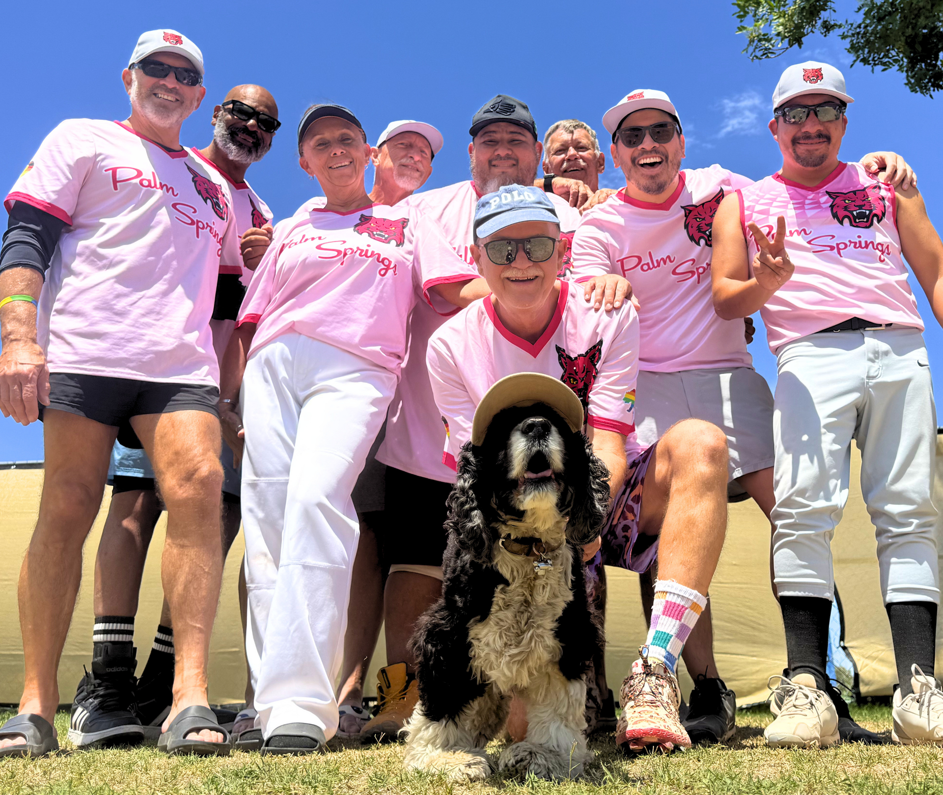 Group of people in pink shirts posing outdoors with a black-and-white dog in the foreground