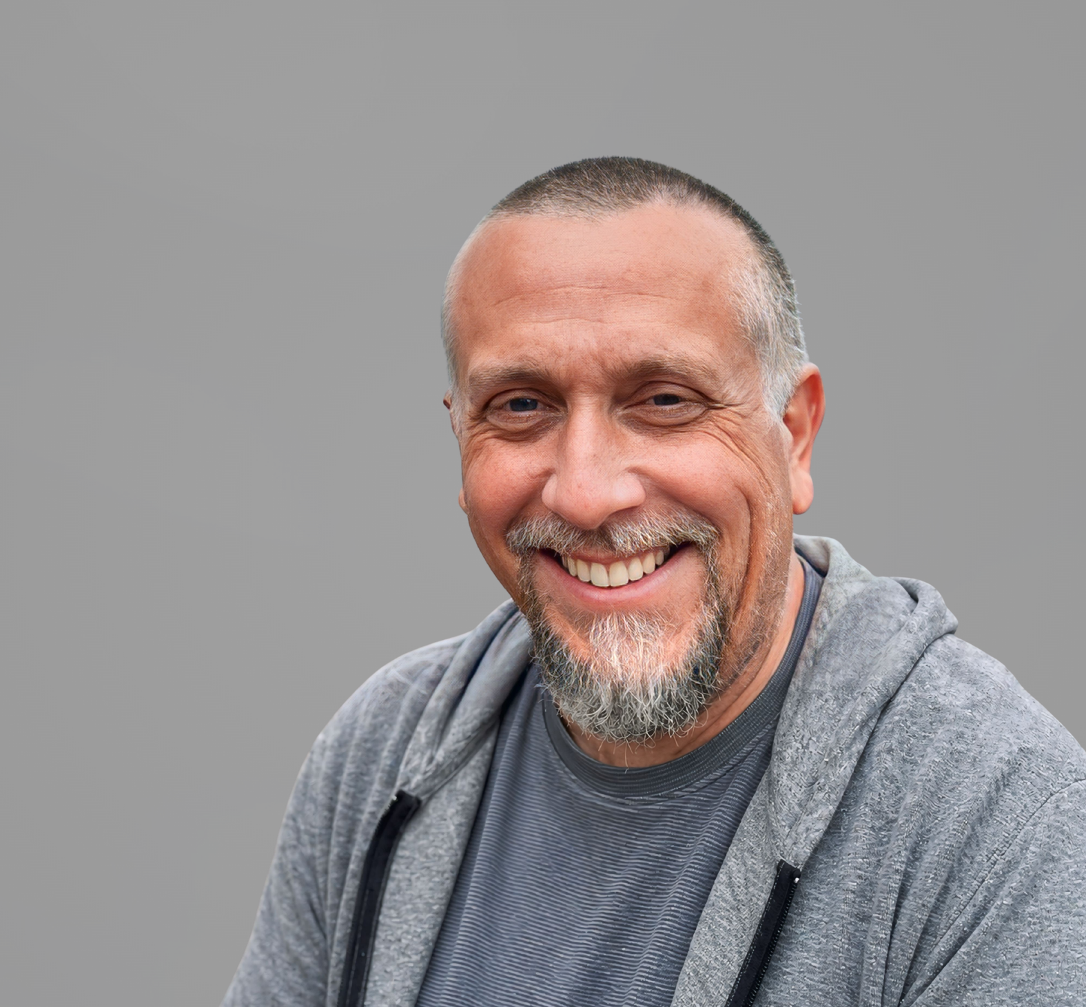 Headshot of Brad Martinson, a man smiling, wearing a trimmed goatee, a gray hoodie, set upon a gray background.