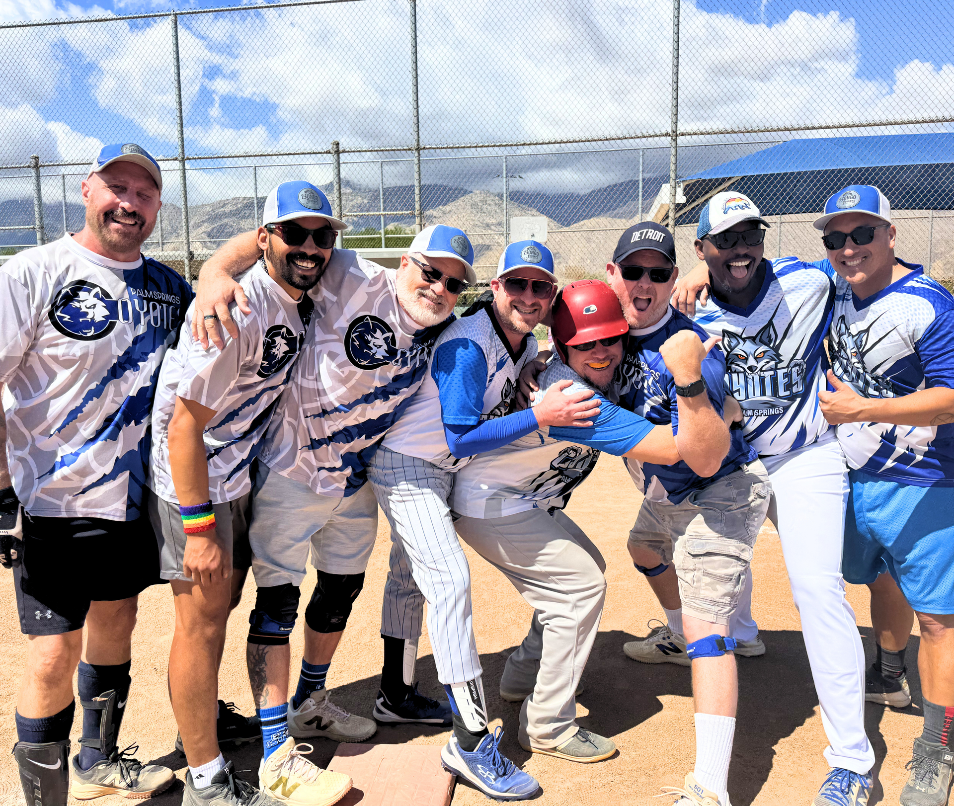 Group of teammates in blue jerseys posing and cheering on a baseball field under a bright sky