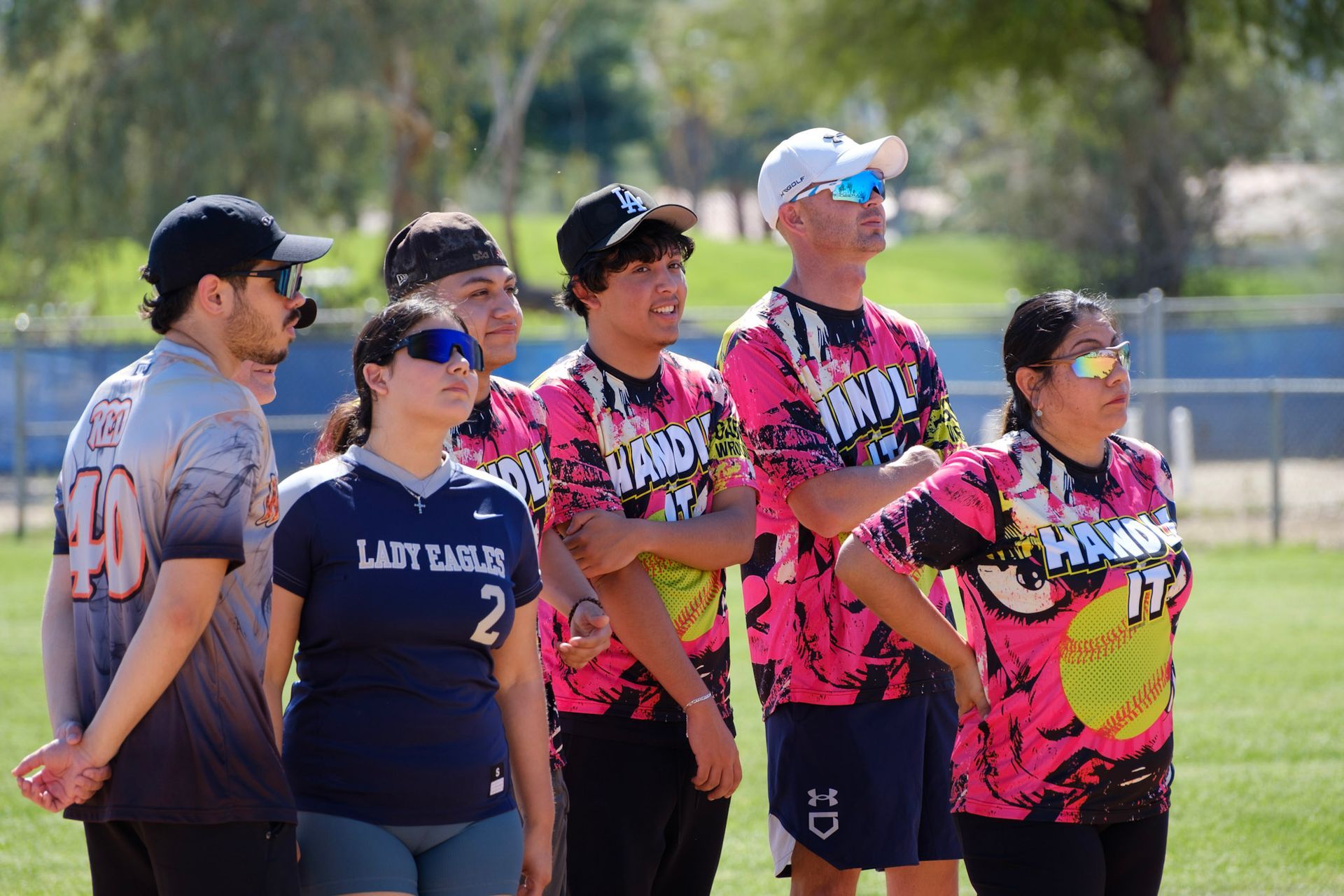 Six people in colorful jerseys standing together on a grassy field, watching something off-camera.