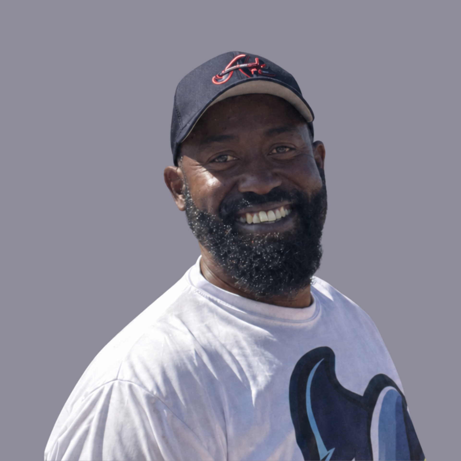 Smiling man in a black cap and sunglasses, wearing a white graphic T-shirt outdoors