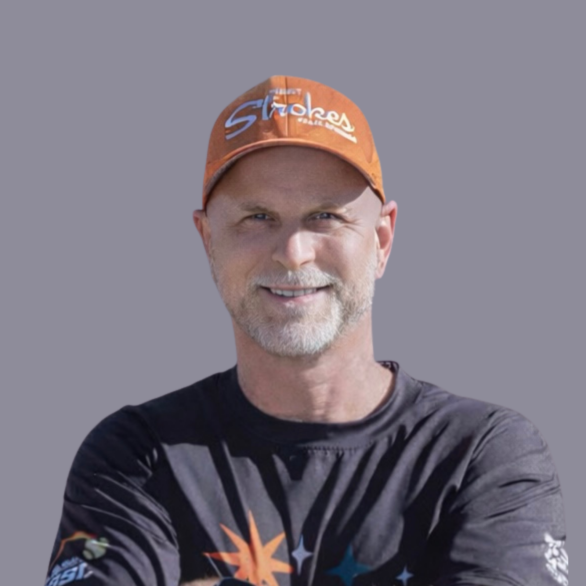 Man wearing an orange cap and black T-shirt, smiling with arms crossed against a gray background