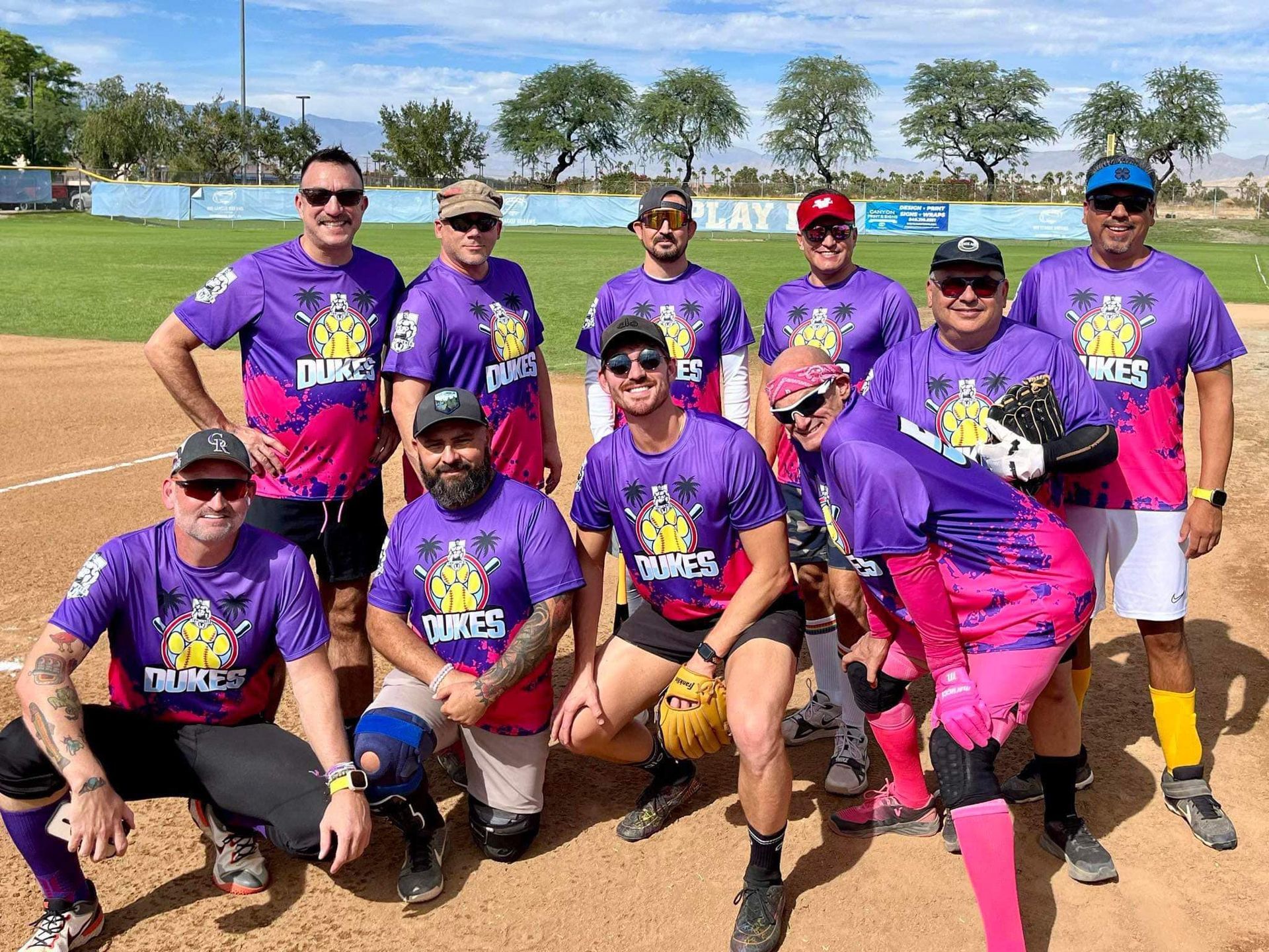 Softball team in purple jerseys posing on a sunny field with bats and gloves