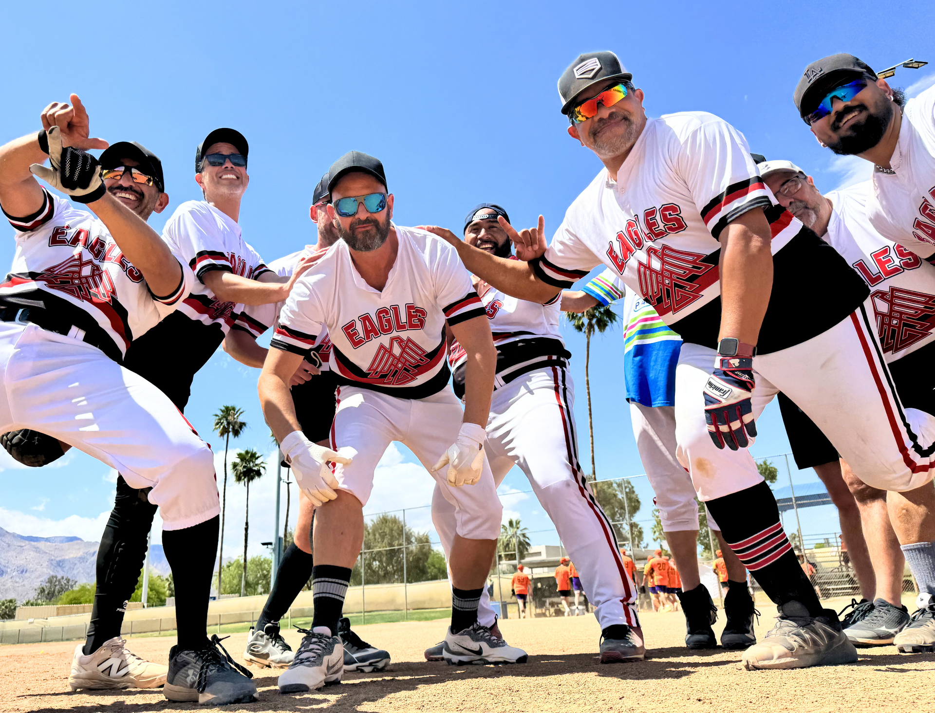 A group of baseball players in white and red uniforms pose in a huddle on a sunny field.