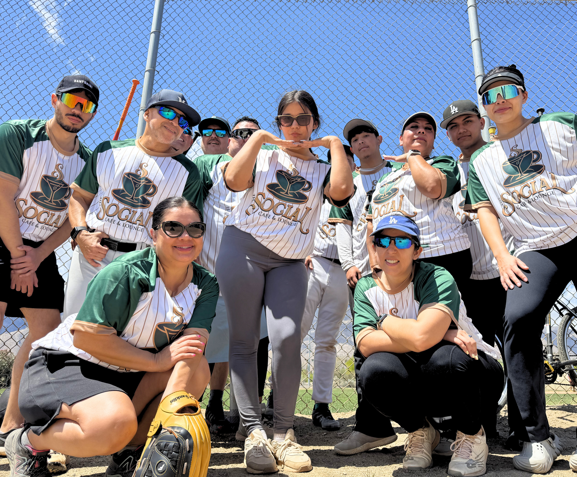 Group of people posing outdoors in matching jerseys and sunglasses, crouching and standing together in sunlight