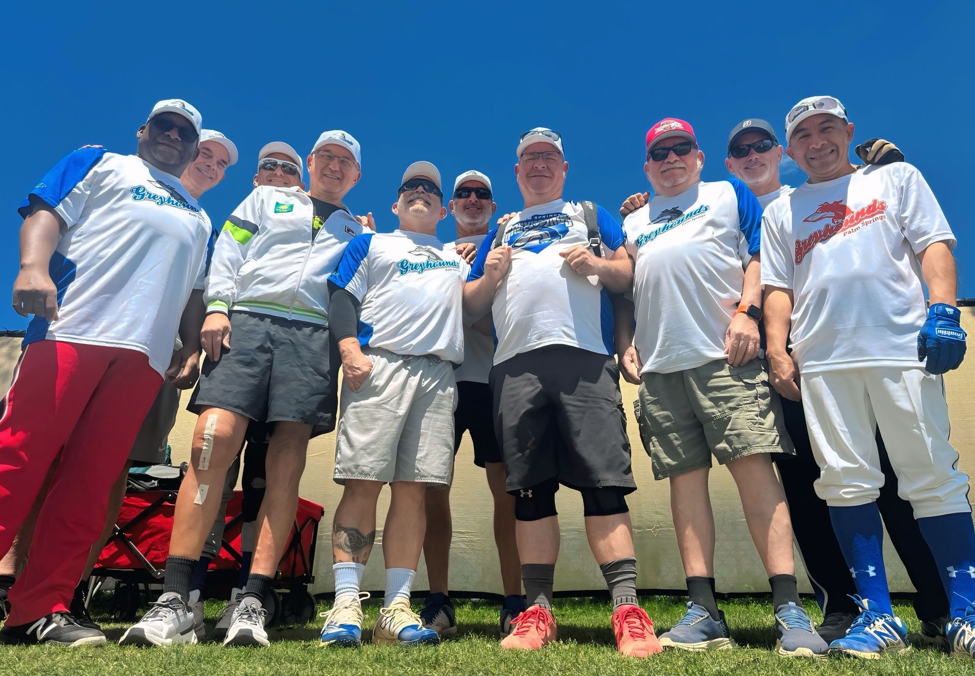 Group of golfers in matching white shirts posing together on a sunny golf course.