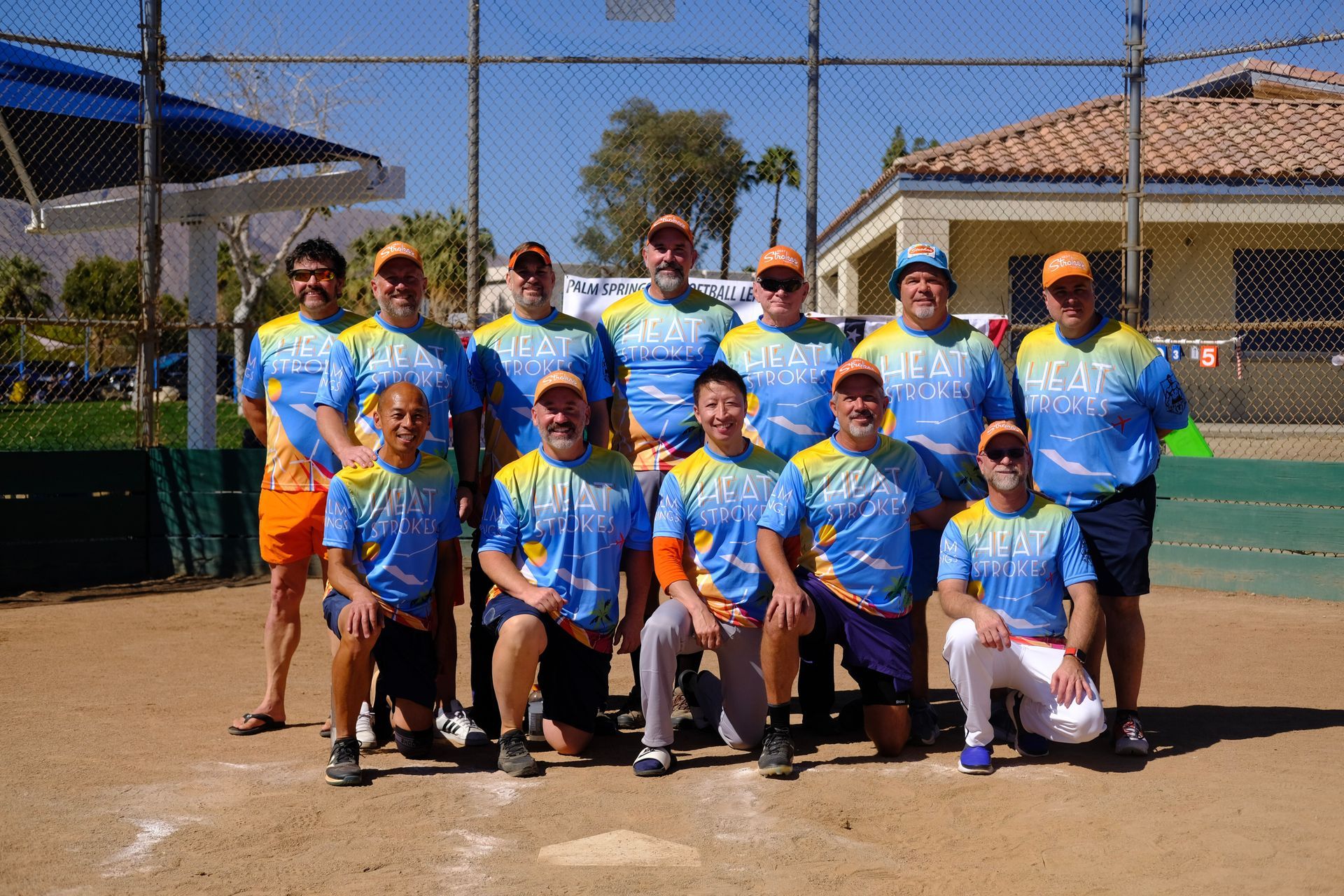 Group of softball players in blue jerseys posing on a field with nets and houses in the background