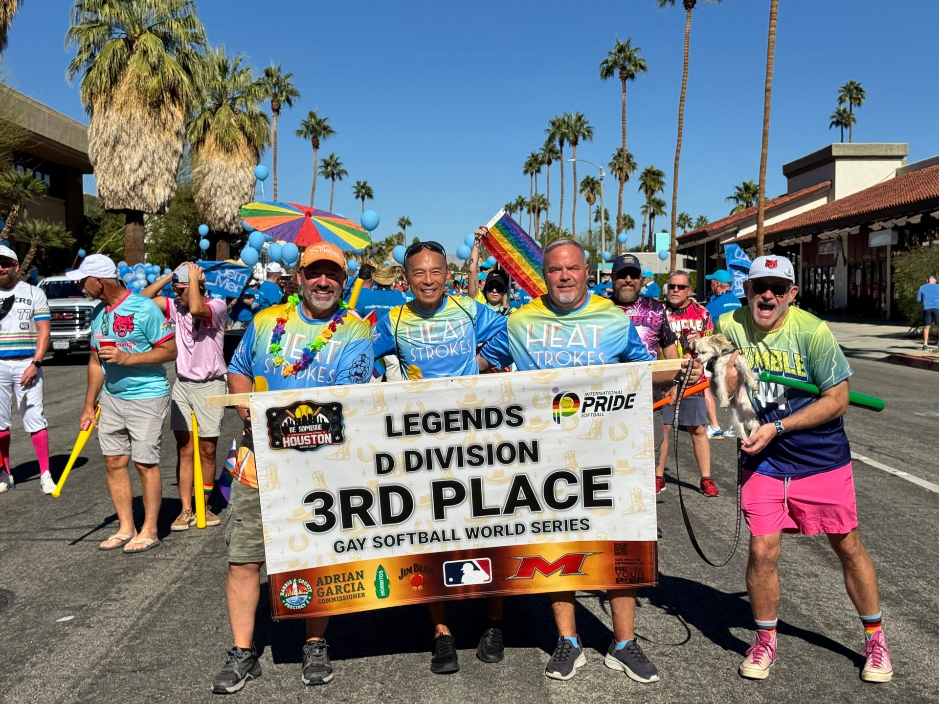 Group in bright shirts holding a “3rd Place” banner at an outdoor race finish line.