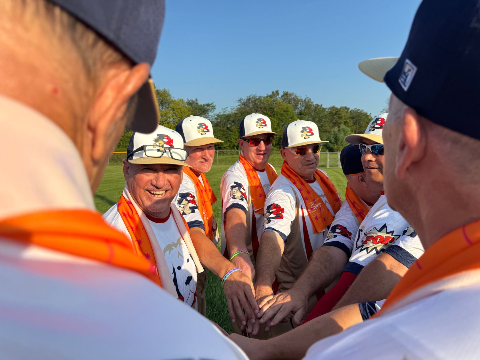 Baseball team huddles on the field, hands stacked together in a circle before the game.