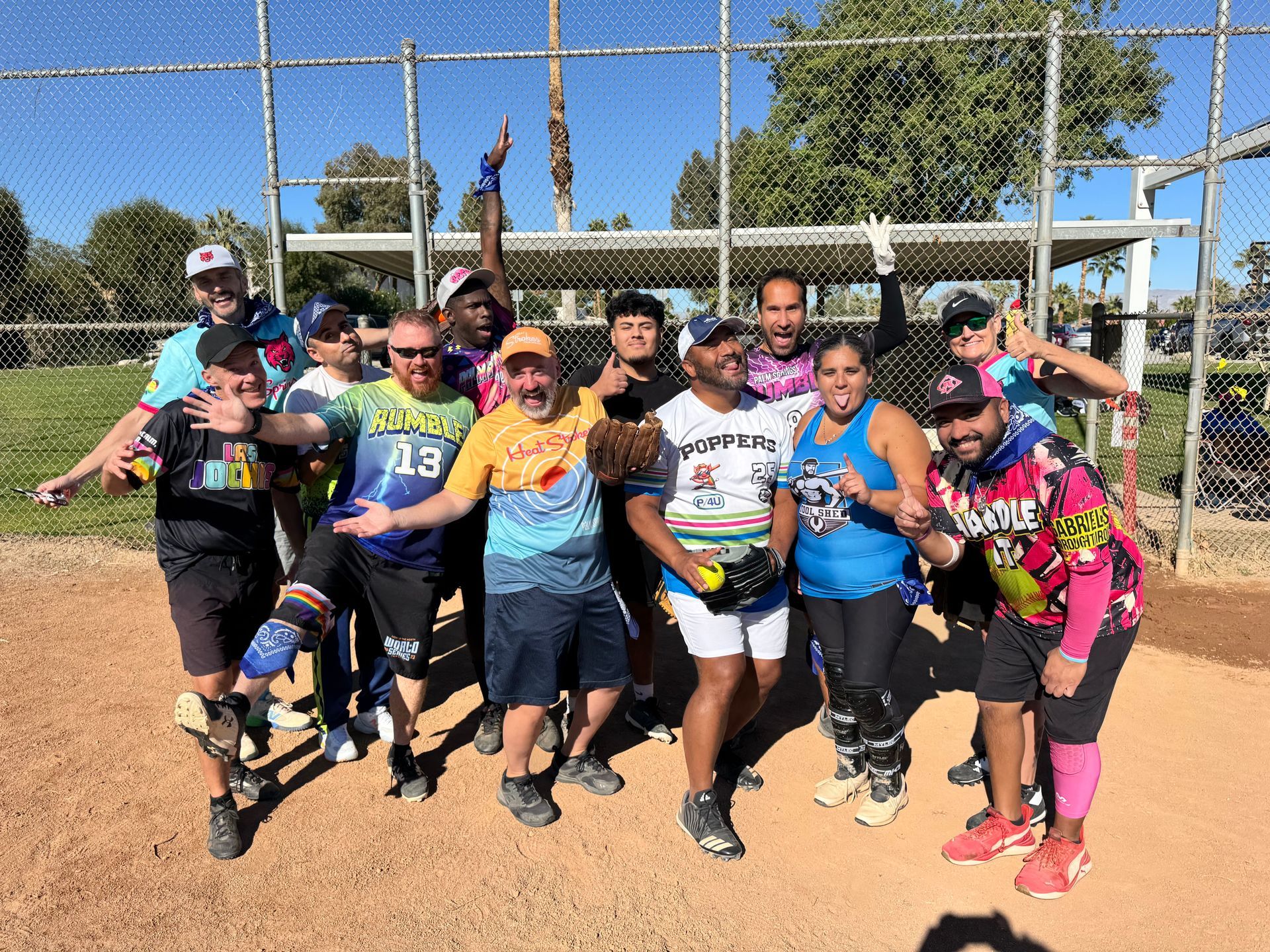 Group of people in colorful jerseys posing on a softball field under a clear sky