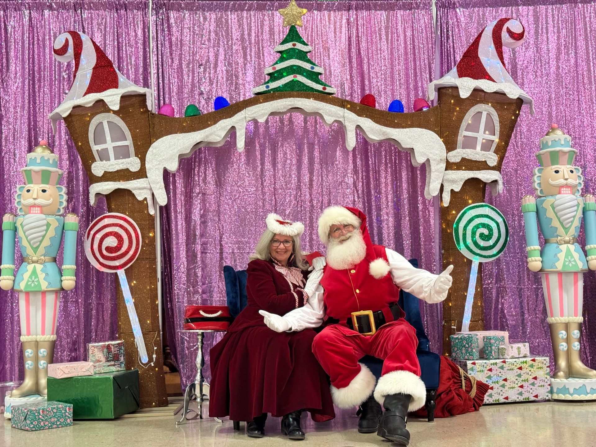 Santa and Mrs. Claus seated on a festive holiday throne with candy canes and gift boxes in a decorated display.