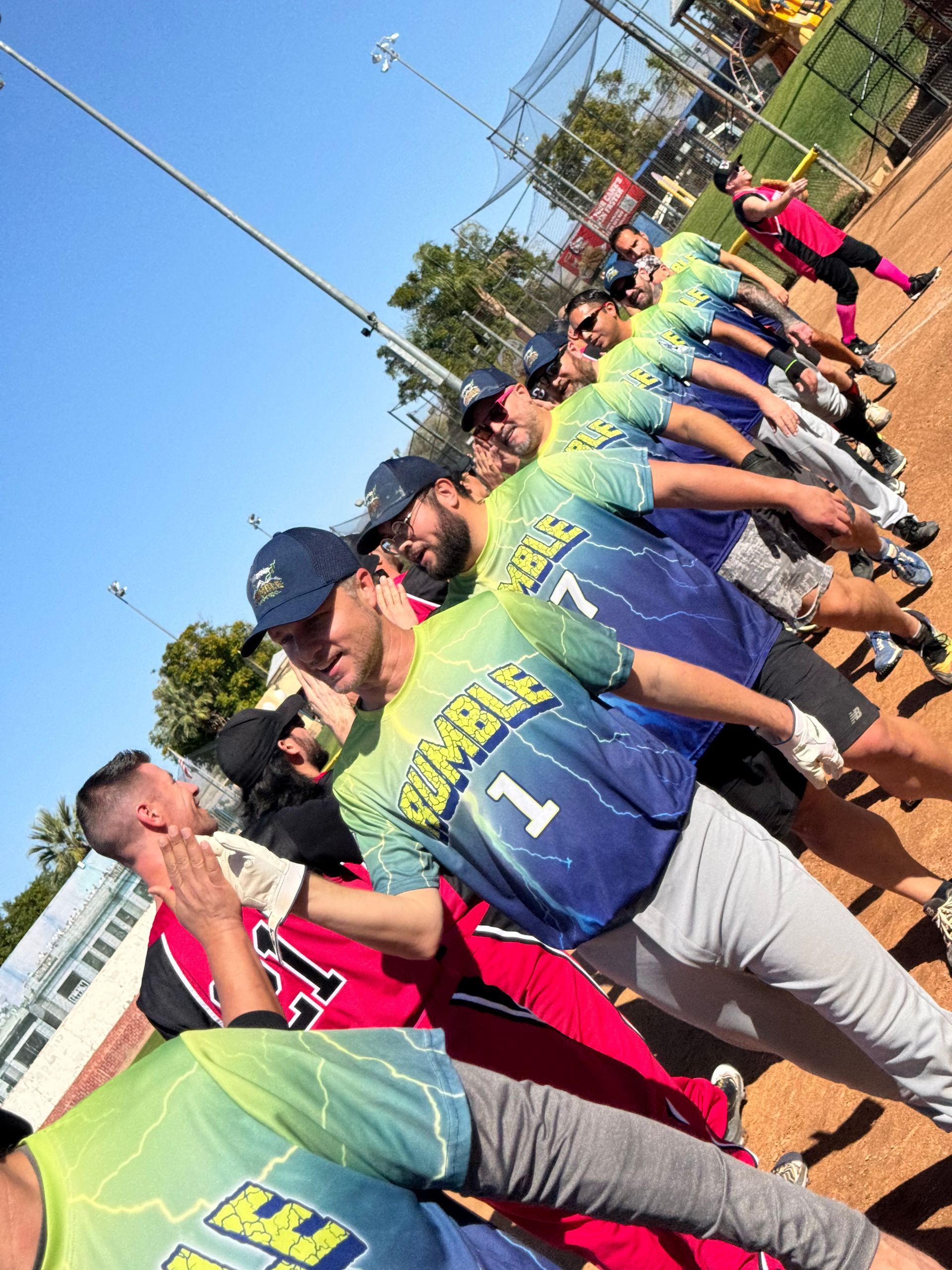 People in colorful shirts lined up outdoors in a sideways group pose under a blue sky.
