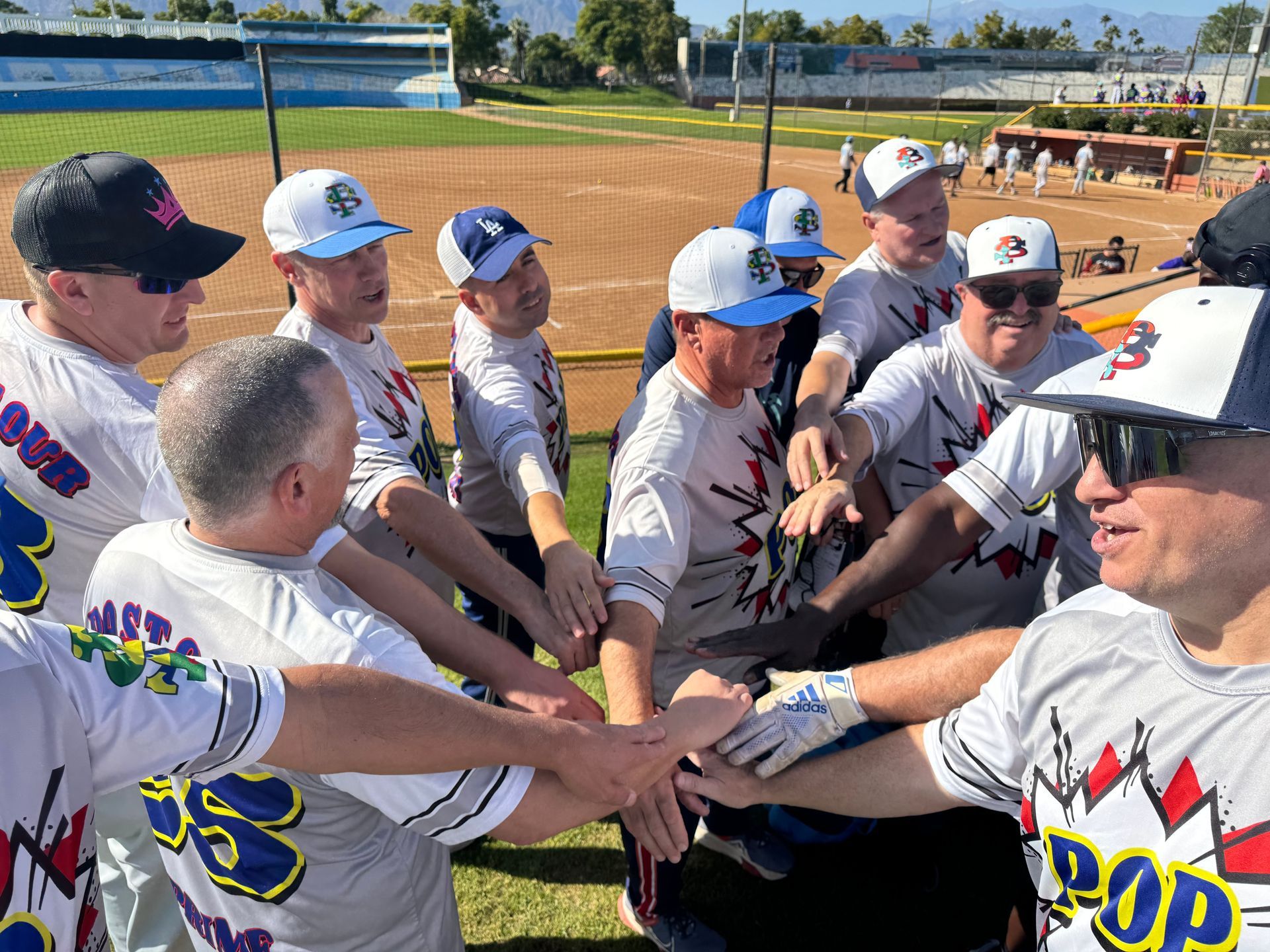 Baseball team huddles on the field, hands stacked together in a circle before the game.