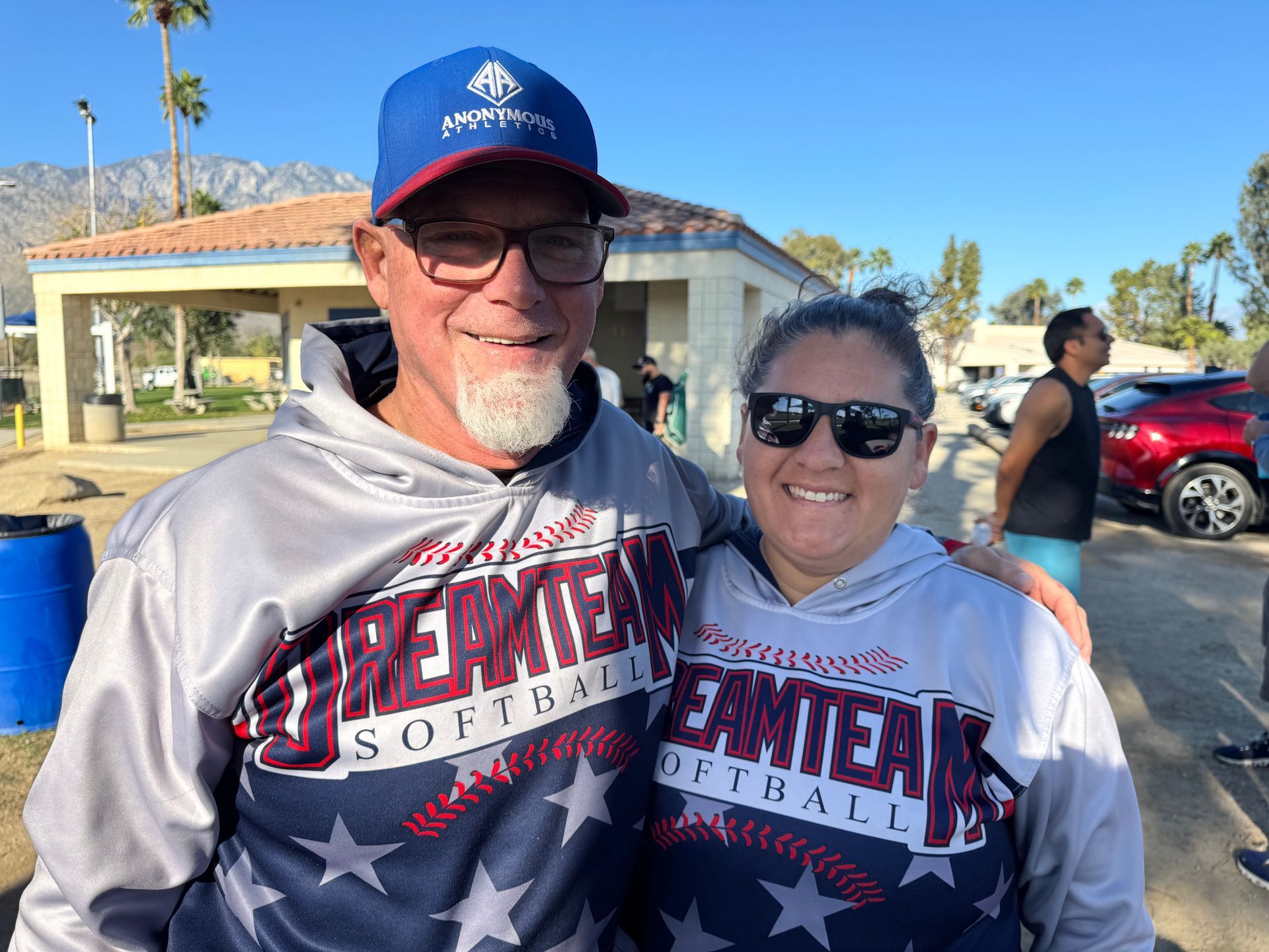 Two smiling people in matching Nevada hoodies and caps standing outdoors in bright sunlight