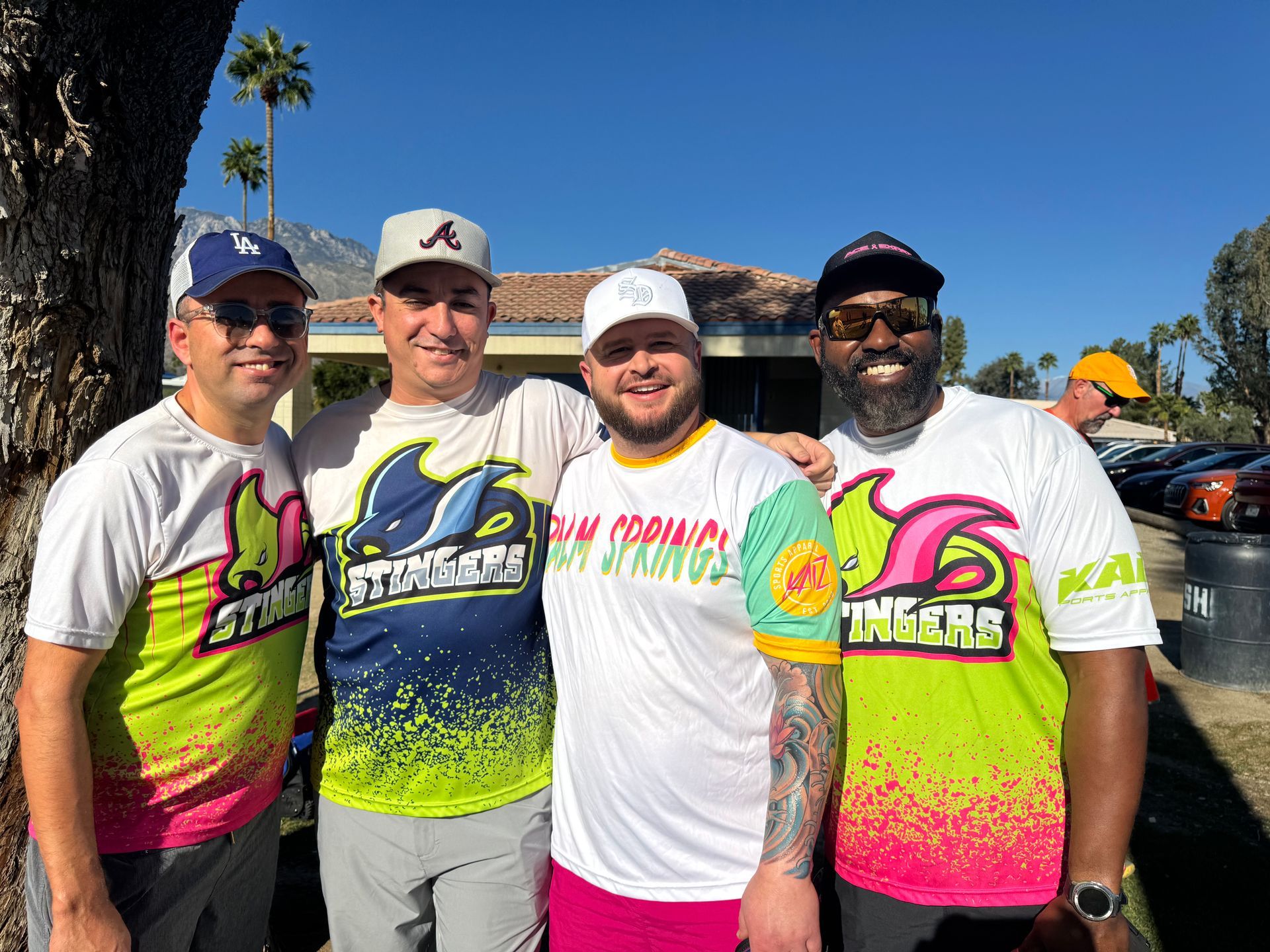 Four men in bright neon racing jerseys pose outdoors under a clear blue sky.