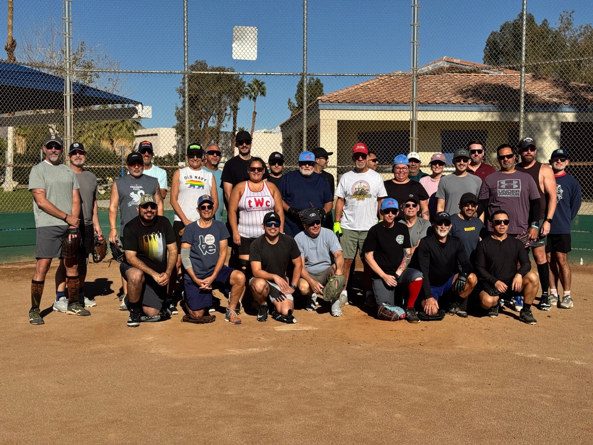 Large group posing on a baseball field, with houses and netting in the background.