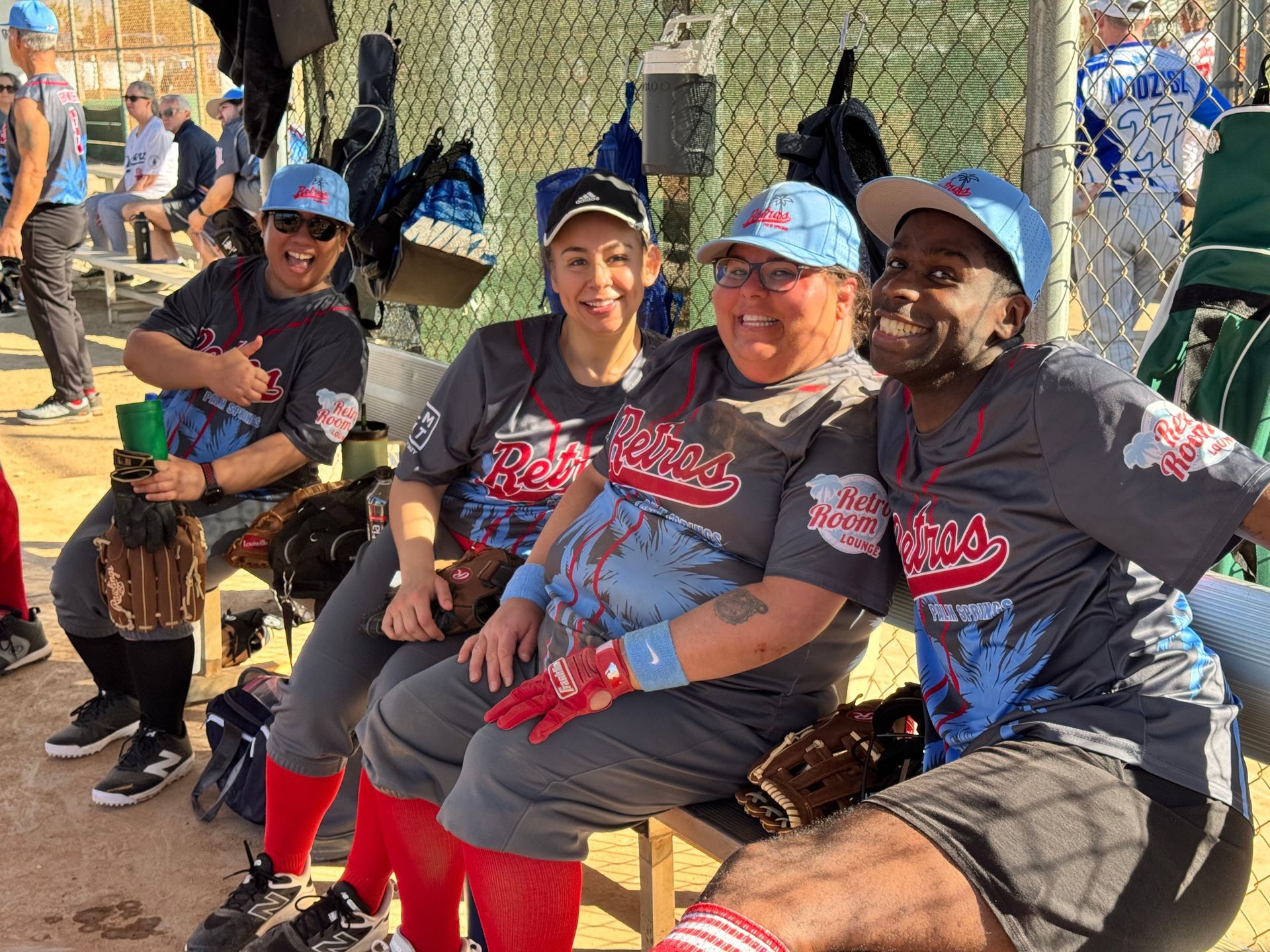 Four people in matching jerseys and caps sit smiling together outdoors on a bench.