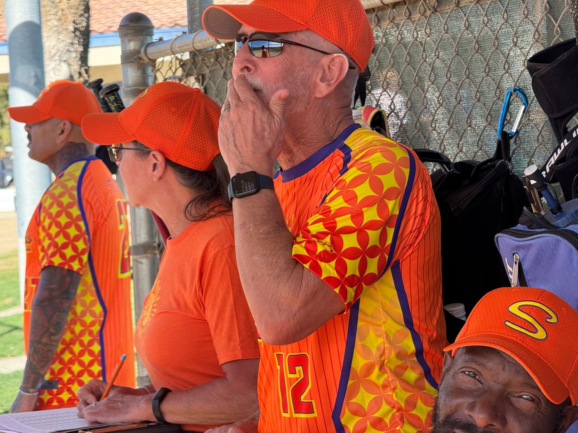 Spectators in bright orange shirts and caps watch from bleachers at a sports game