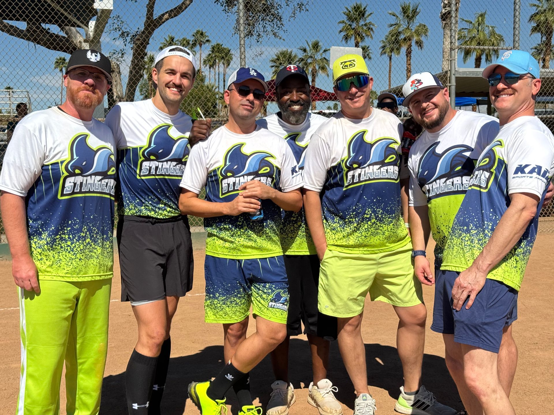 Seven runners posing outdoors in matching white, blue, and neon green race shirts and shorts