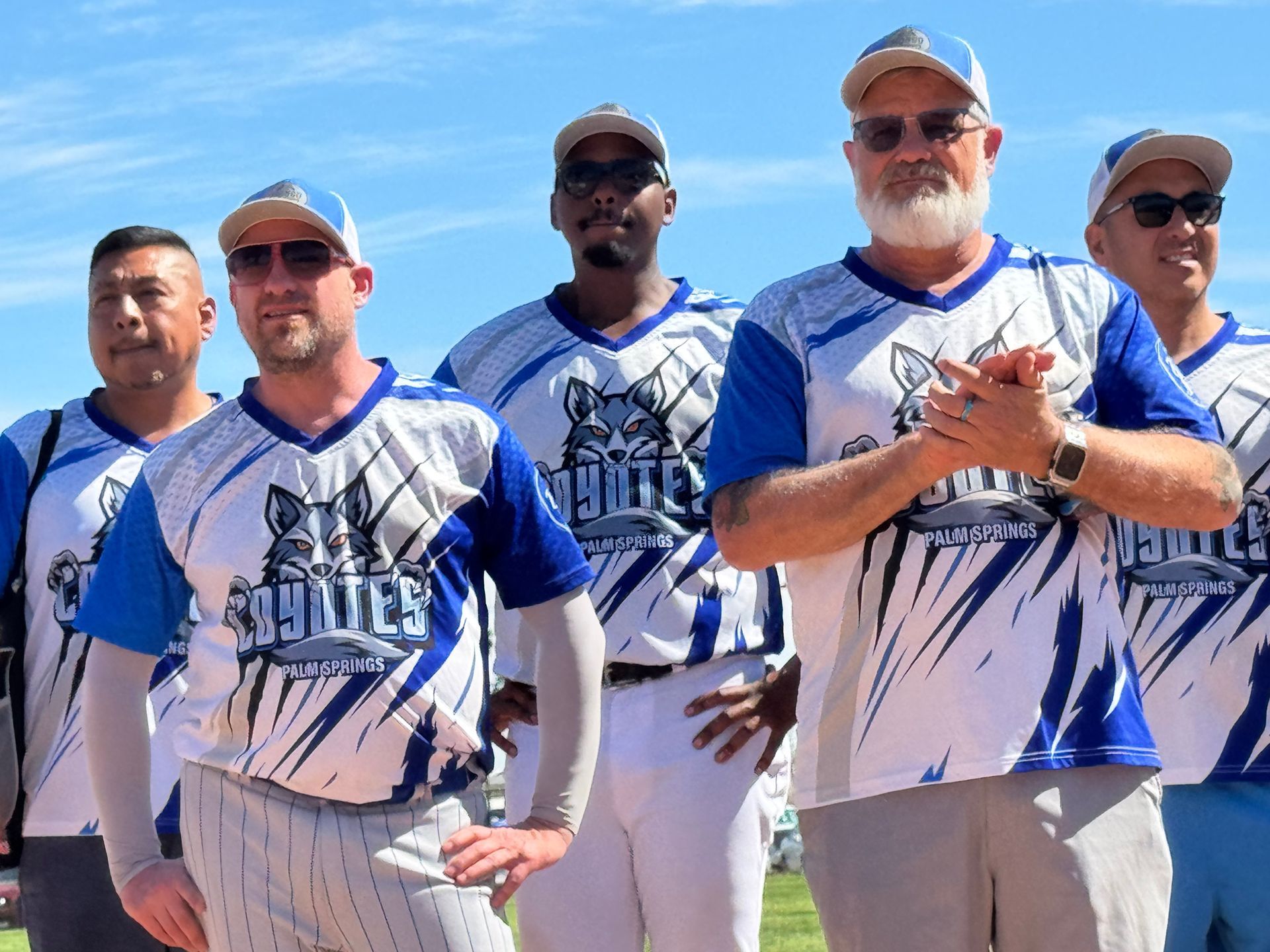 Five men in blue-and-white sports shirts standing outdoors under a clear sky.