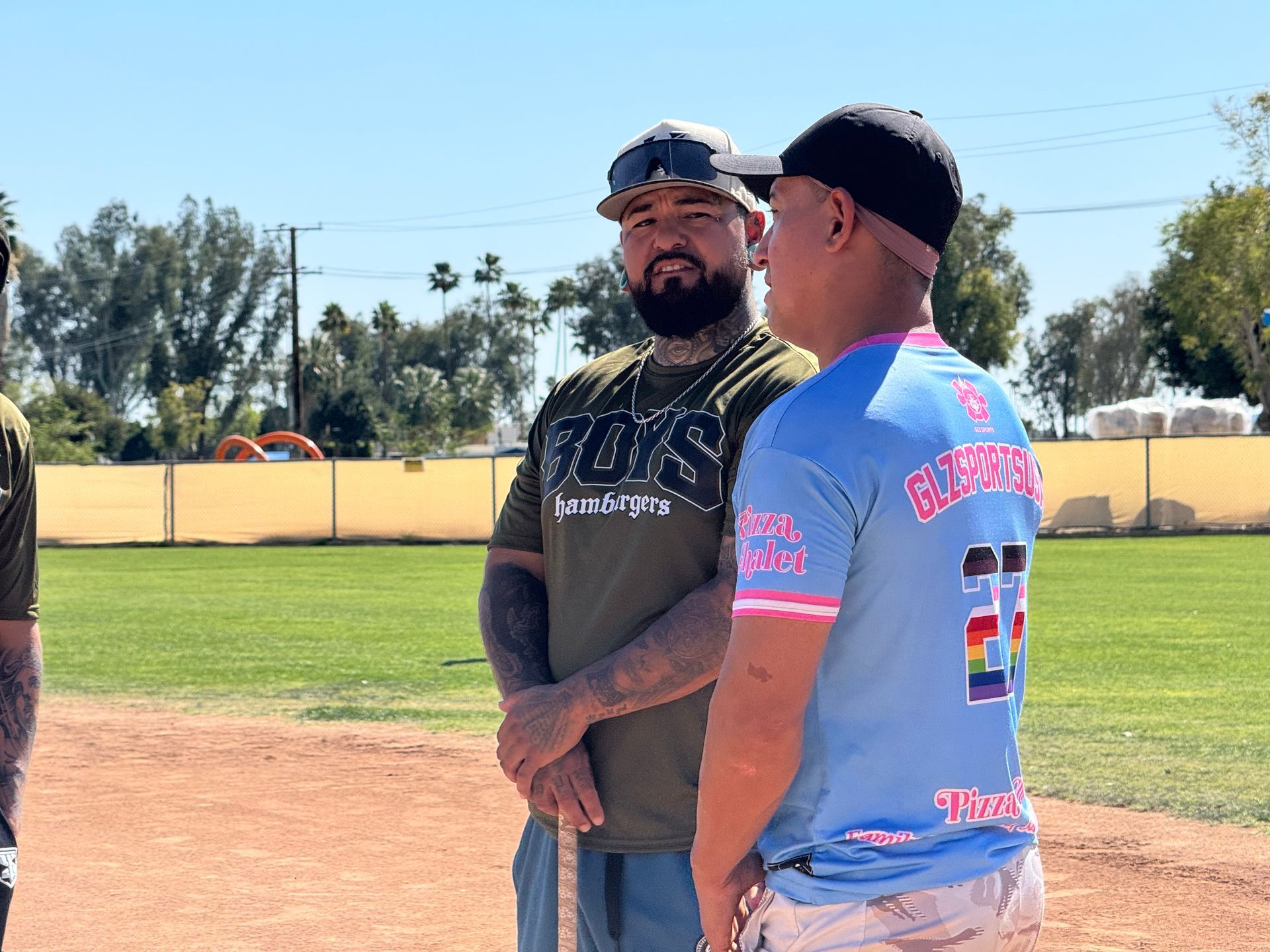 Two men standing and talking on a baseball field under a sunny sky