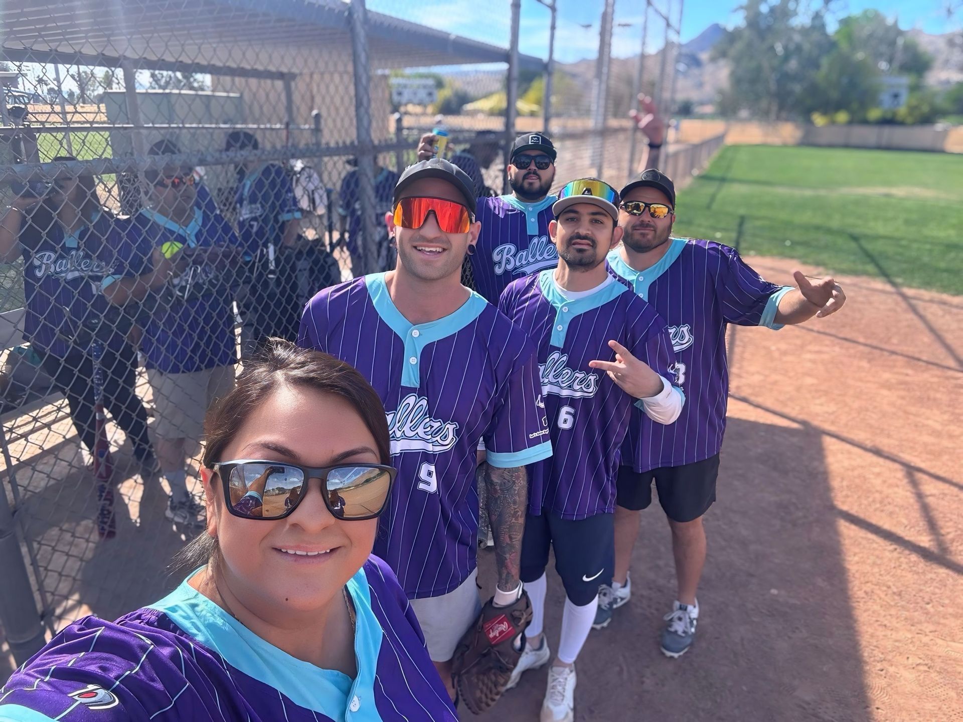 Softball team in purple uniforms posing on a sunny field with chain-link fencing nearby