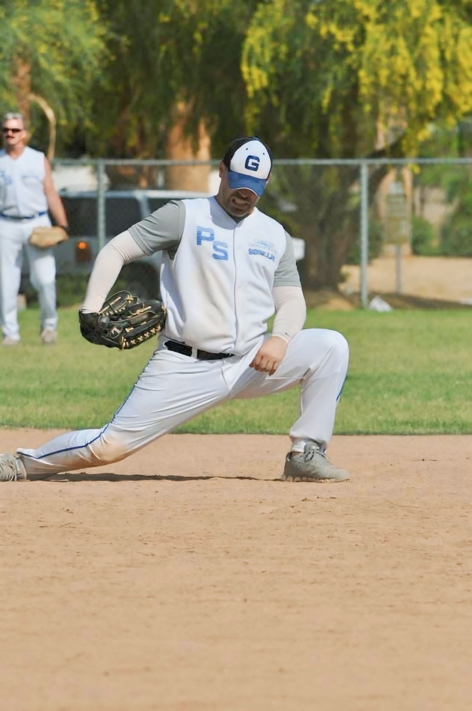 Baseball player in white uniform lunges to field a ground ball on a dirt infield.