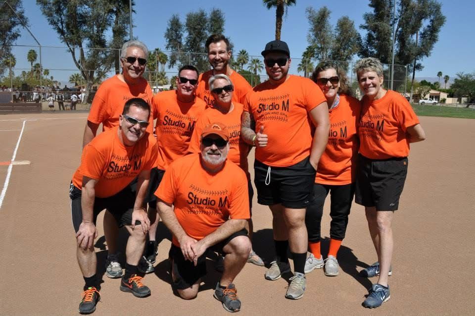 Group of people in orange shirts posing on an outdoor track, smiling in sunlight.