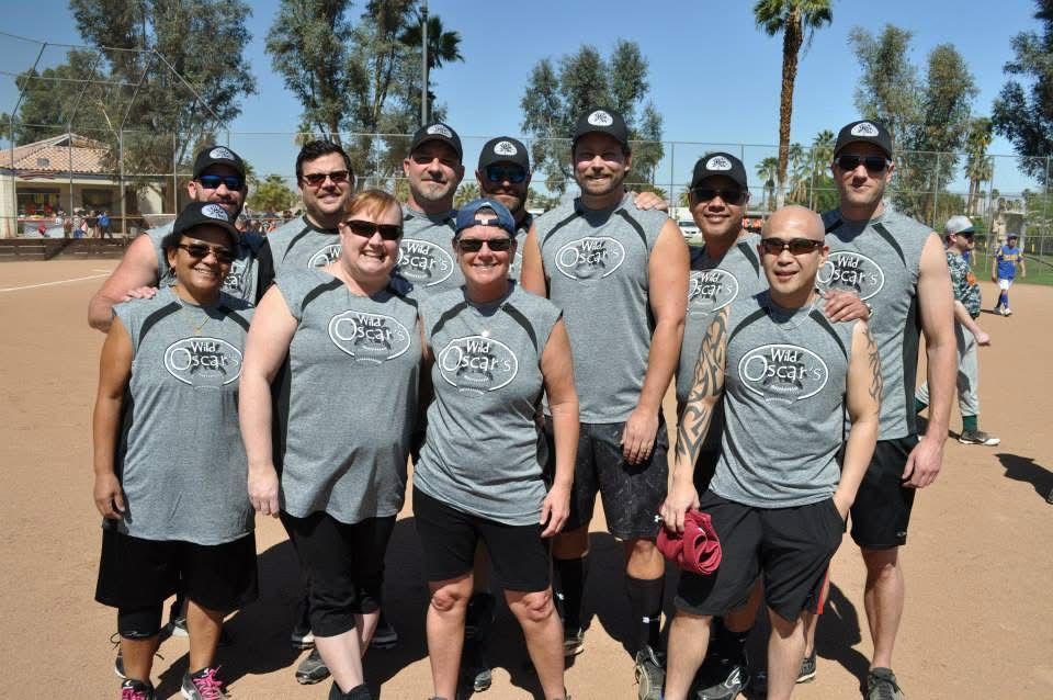 Group of hikers in gray shirts and black shorts posing outdoors on a sunny dirt path.