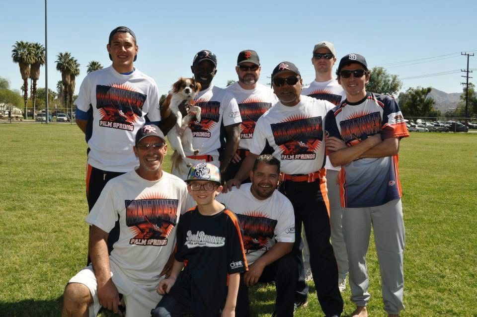 Group of people posing on a grassy field, some in matching shirts, under bright daylight.