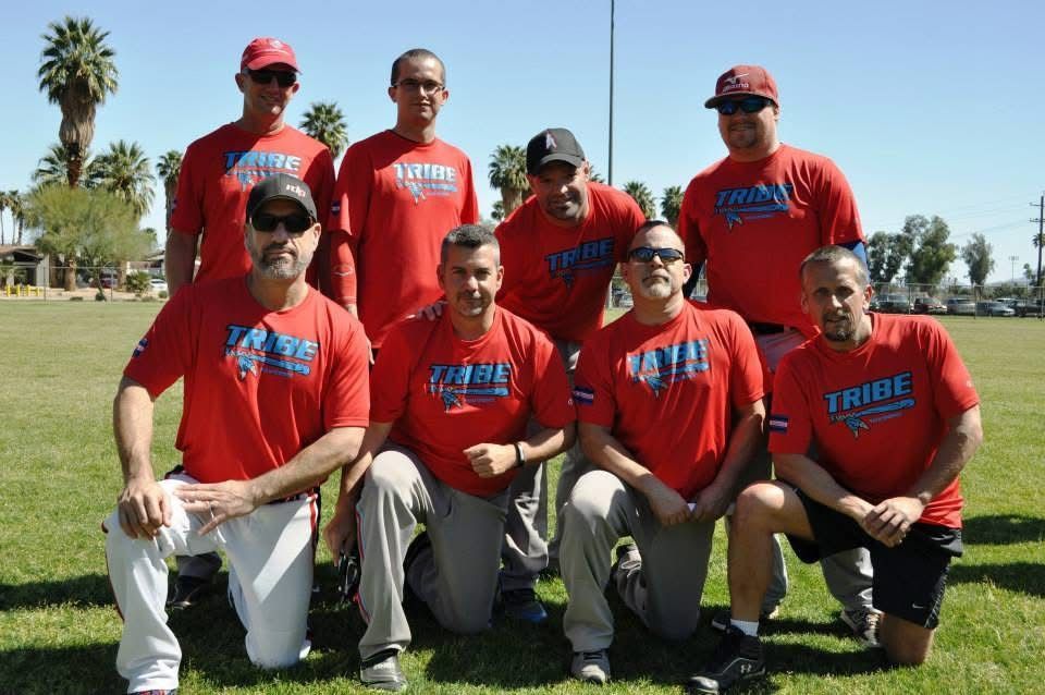Group of eight people in red shirts and caps posing on a grassy field, kneeling and standing in two rows.
