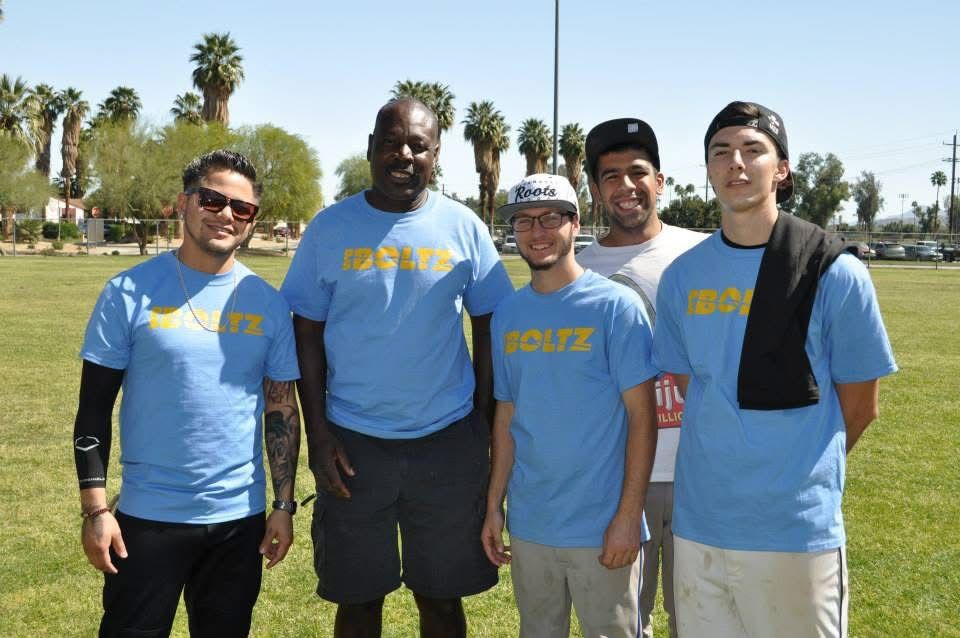 Five people in blue shirts standing together outdoors on a sunny field.