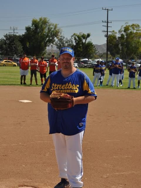 Baseball player in blue and white uniform standing on the field holding a glove, with teams lined up behind him.