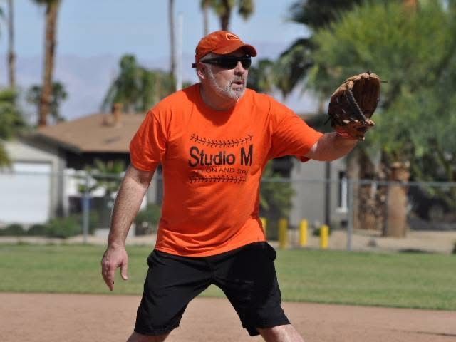 Man in orange shirt and cap preparing to catch a baseball on a field