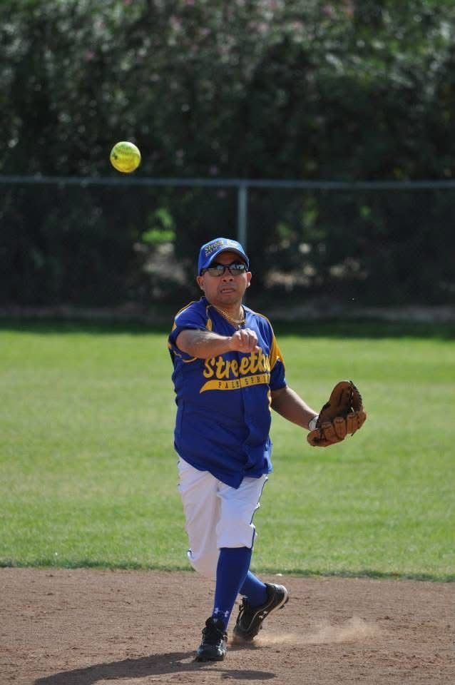 Youth softball player in blue uniform pitching on a field with the ball midair