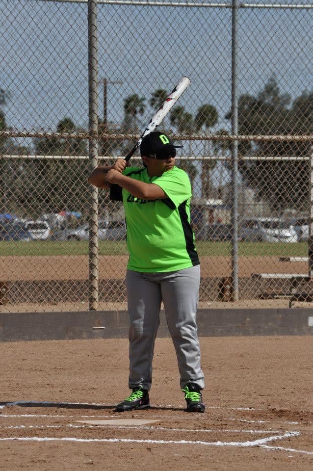 Softball player in neon green jersey stands at home plate, holding a bat ready to swing.