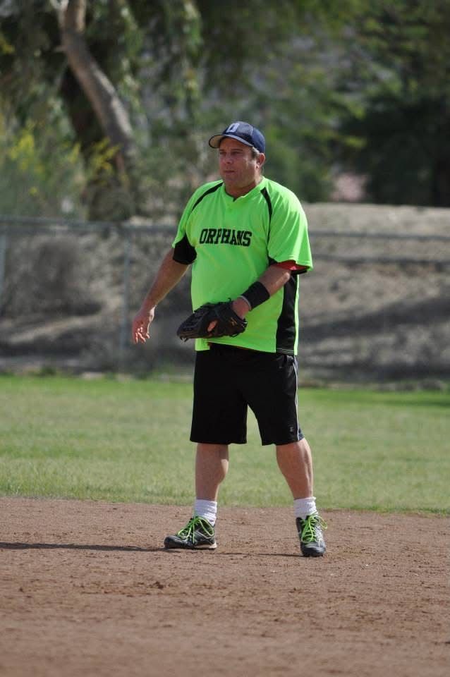 Softball player in neon green jersey and black shorts standing on a dirt field with a glove.