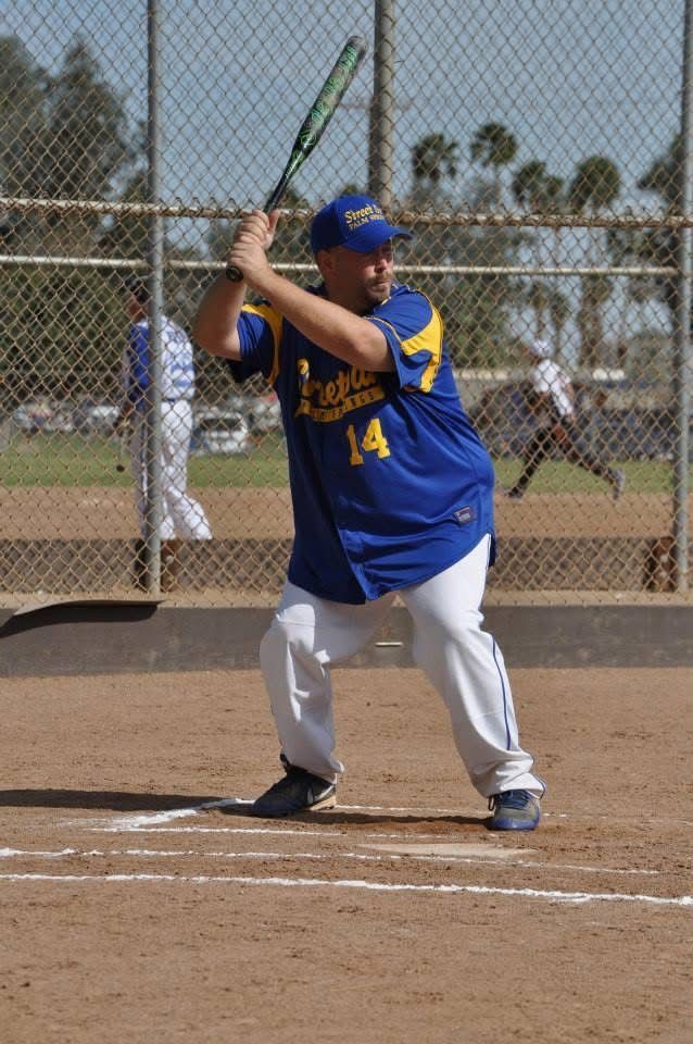 Baseball batter in blue uniform at the plate, holding a bat ready to swing, with a chain-link fence behind him.