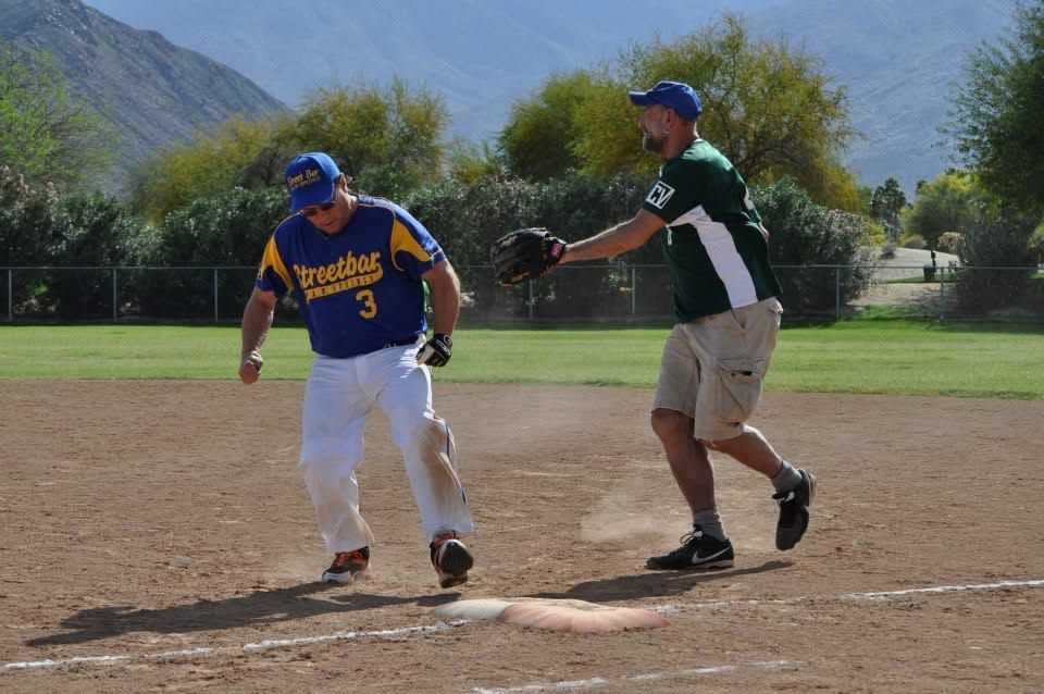 Two baseball players near a base, one in blue and white stepping on the bag, with mountains in the background.