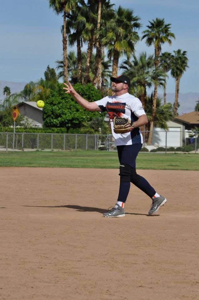 Baseball player in white and black uniform pitching on a dirt field with palm trees in the background