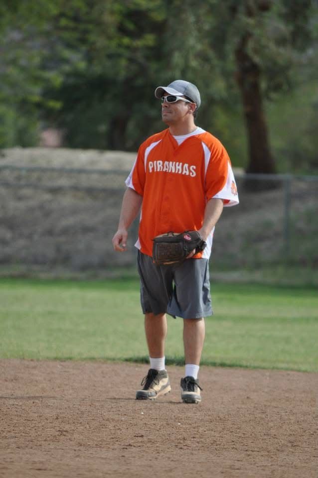 Baseball player in orange jersey standing on a mound, looking to the side, holding a glove and ball.