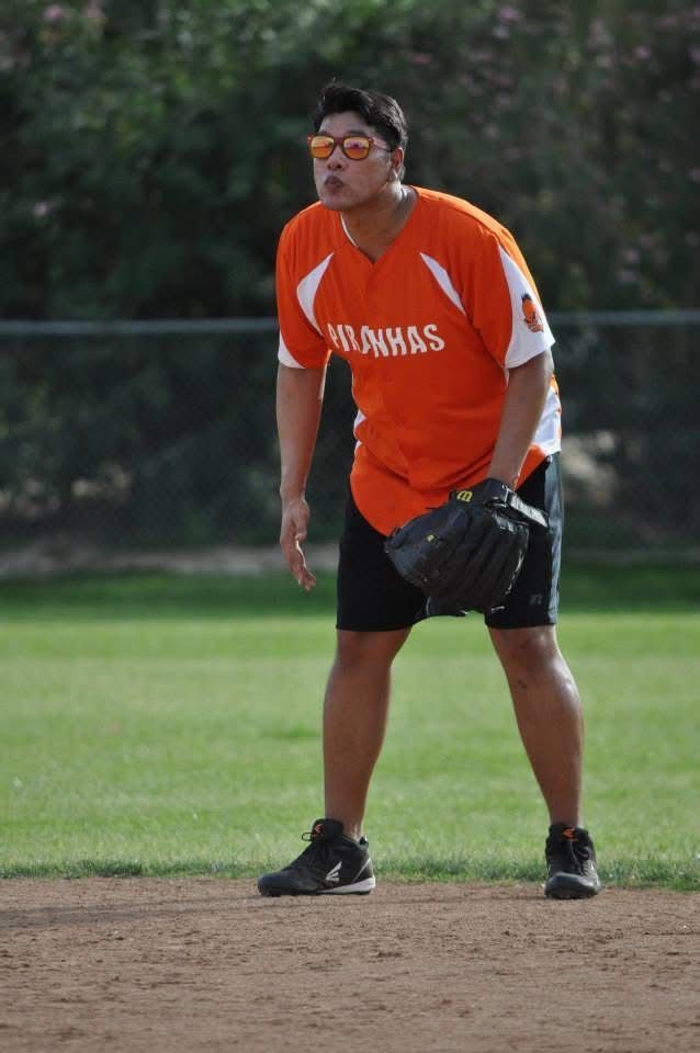 Baseball player in orange jersey and black shorts fielding on a dirt infield